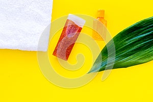 Sun protection products. Bottles with cream or lotion near towel and palm leaves on yellow background top view copy