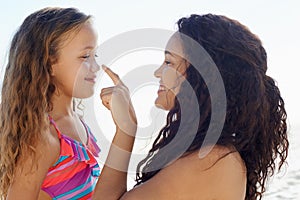 Sun protection is very important. A young girl poking her mothers nose while theyre at the beach.
