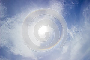 Sun with rainbow ring around it with blue sky and clouds