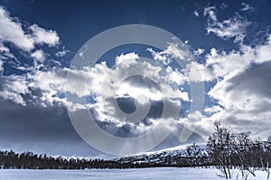 Sun rays breaking through the clouds above birch forest and a snow covered mountain, at Joesjo village, Winter Scandinavian