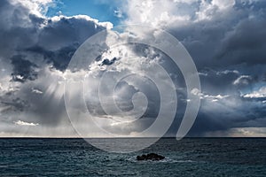 Sun rays through dark rain clouds over the sea