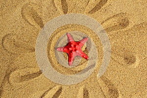 A sun with rays is drawn on the sand, and a sea red star was placed.