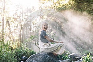 Sun rays illuminating a woman with happy expression sitting ina rock in the rainforest