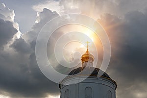 Sun rays make their way through the thunderclouds illuminating the golden cross on the dome of the old church