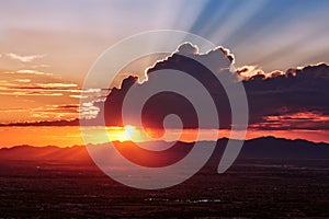 Sun rays shine behind a cumulus cloud at sunset