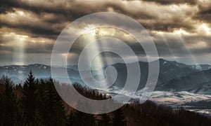 Sun rays shining through dark clouds on the hills