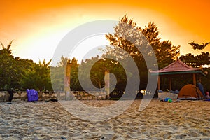 The sun rises on the beach with a pavilion on the sand.