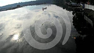 Sun rises on lake boatman paddle his way toward the shore of polluted lake. Silhouettes