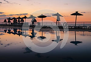 The sun rises by the pool near the hotel in Mallorca. Sun umbrellas reflected in the water