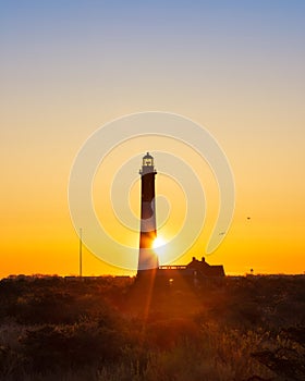 Sun rising from behind a tall lighthouse, creating a golden star burst.