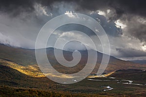 The sun`s rays break through the dark gray clouds. Impressive view of the mountains of Sarek national park in Swedish Lapland.