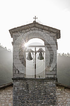 The sun`s rays filter through the bells of the Church of San Montano in Roccaporena, Perugia, Italy