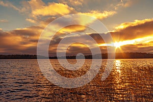 Sun`s rays make their way through the clouds above the lake at sunset. Beautiful evening landscape background