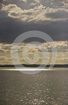 The sun`s rays make their way through the clouds and illuminate the lake