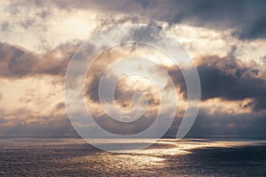 The sun`s rays make their way through dramatic dark clouds over the sea, patches of light on the water