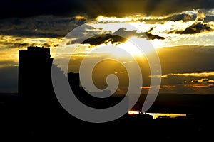 The sun`s rays of the setting sun against a stormy sky in a big city, the outlines of buildings in the background of the bright