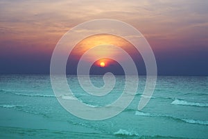 Sun set on green water sea and waves on orange blue sky background