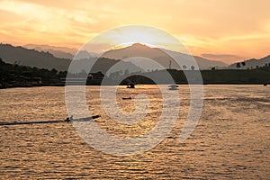 The sun sets behind the mountain, lighting up the last rays of a fishing boat, which is anchored in a tropical bay . Thailand.