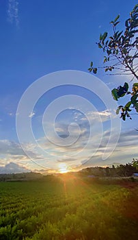 the sun sets in a clear blue afternoon sky with rays that shoot up on the hills commonly called & x22;bukit barisan selatan& x22;