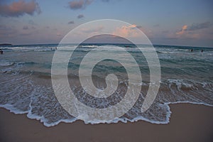 Sun sets, creating a pastel sky, beachgoers bask in the tranquil ocean waves