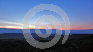 The sun sets in the great Rift Valley in Kenya. At dusk, hills and valleys covered in rainforest are visible.