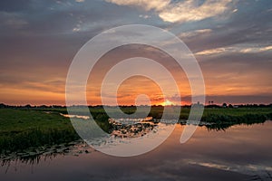 The sun sets on the horizon of the dutch countryside. A beautiful colored sky is reflected in the water of a lake.