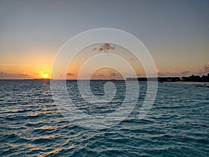 The sun sets over the ocean next to an island in the Maldives