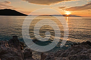Sun is setting behind Skiathos island with some sea rocks in foreground at Kastani Mamma Mia beach, island of Skopelos