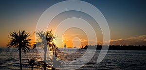 Sun setting of coast of Key West with sailboats, palm trees and clouds