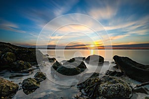 The sun setting on the horizon along a rugged coastline. Green algae on rocks as the tide recedes.