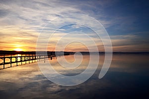 Sun setting with long jetty extending out in lake