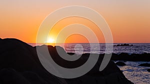 Sun setting on the ocean, behind a large rock in silhouette