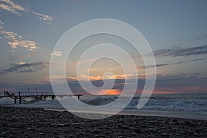 Sun setting over Batumi beach pier, as powerful waves roll in, and a very colorful sky is reflected on the beach