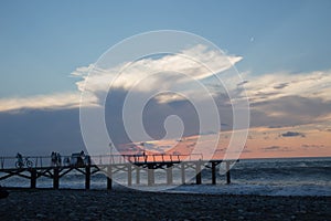 Sun setting over Batumi beach pier, as powerful waves roll in, and a very colorful sky is reflected on the beach