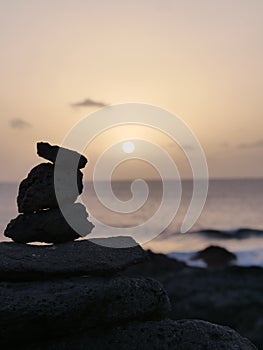 Sun setting over a calm sea behind the silhouette of rock pile looking like a rabbit.