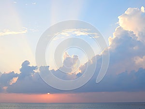 Sun Setting over Ocean with Rays through Clouds in Blue Sky