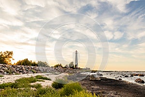 Sun is setting on the shore near lighthouse.