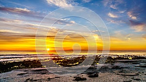 Sun setting under orange sky over the horizon of the Atlantic Ocean at Camps Bay near Cape Town