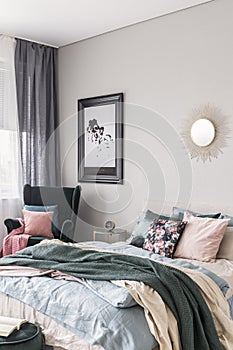 Sun shape like mirror and map in black frame on grey wall of fashionable bedroom interior with king size bed with cozy bedding