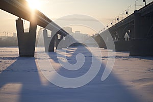 The sun shines across the city bridge over the frozen river on a sunny day.