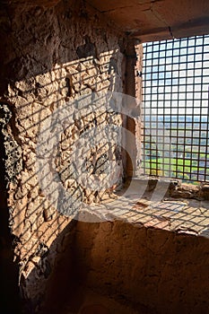 Sun shines through an old castle window with bars with shadows on the wall