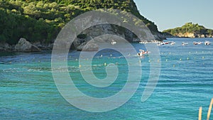 Sun shines to calm blue sea at Liapades bay, boats moving slowly in distance, rocky cliffs with trees background