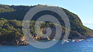 Sun shines to calm blue sea at Liapades bay, boats waiting in distance, rocky cliffs with trees background