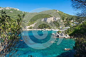 Sun shines to calm blue sea at Liapades bay, view from small rocky cliff near, green coniferous trees and bushes in