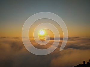 The sun shining above the clouds on a cliff photo