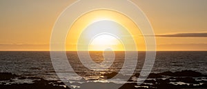 Sun shining brightly on horizon at sunset over ocean with golden reflections