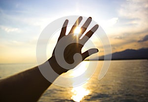 Sun shining through the fingers of the hand on the sea background