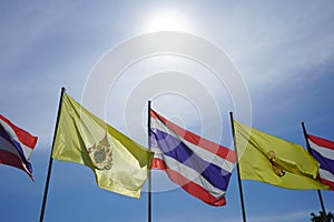 The sun is shining light over Thai national flags and His Majesty King Vajiralongkorn flags