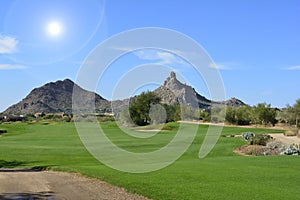 Sun shining over a green golf fairway with mountains and a blue sky