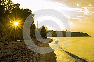 Sun shining trough coastal trees Chalkidiki beach at sunrise Aegean Sea Greece